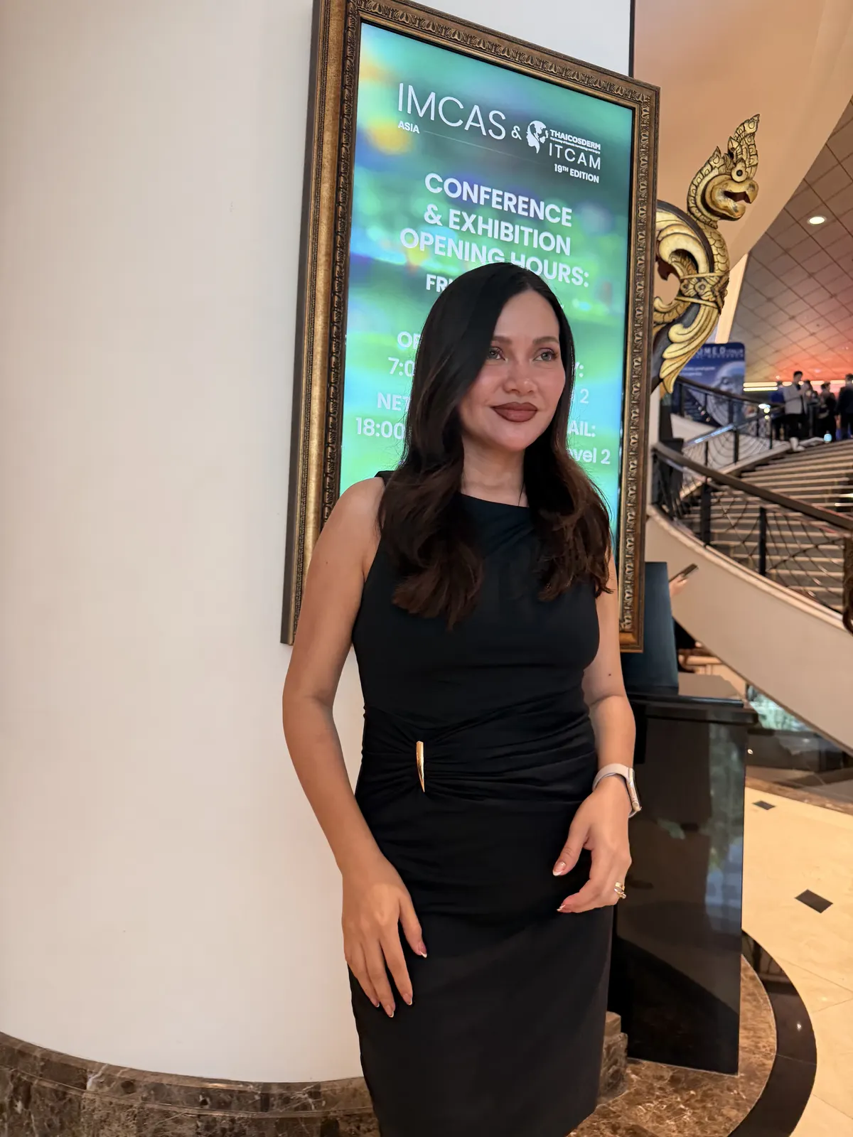 La Dra. Marioly Morales junto al cartel de horarios de IMCAS Asia 2026 en Bangkok
